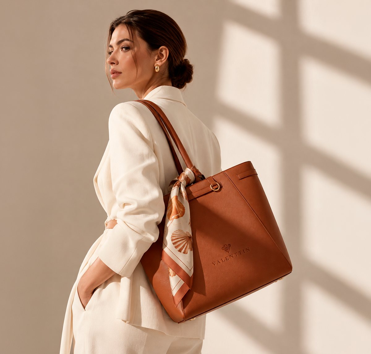 Mulher com bolsa de couro caramelo da marca Valenttin, com o monograma gravado, identidade visual criada pelo Estúdio Fábio Cambréa